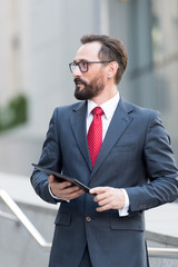 Confident bearded man looking into the distance while standing with tablet