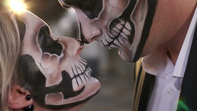 Close-up of the face of a couple in love with Halloween makeup in the form of a skeleton, they look at each other terrifyingly. Halloween loving couple with skull makeup looking at each other.