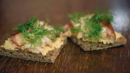 Rye bread canapes with smoked arctic char, cream cheese and dill toppings on brown wooden table. Copy space.