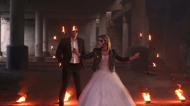 Scary couple with creepy makeup on Halloween with fire and burning torches in an abandoned mansion. Zombie bride and groom. Halloween and fire.