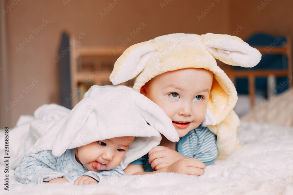 Wall mural Portrait of toddler boy and baby girl wearing rabbit ears smiling.