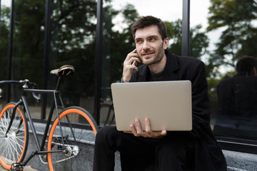 Smiling man dressed in coat sitting at the street