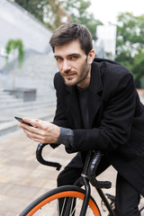 Handsome young man dressed in coat leaning on a bicycle