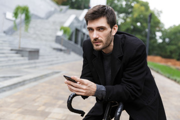 Attractive young man dressed in coat leaning on a bicycle