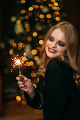Portrait of young attractive celebrating woman holding sparkles. Background of christmas tree