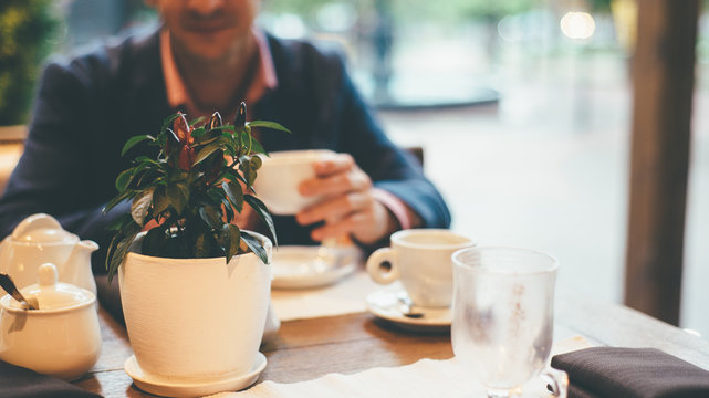 Close up image of blurred man with coffee cup sitting behind focused plant