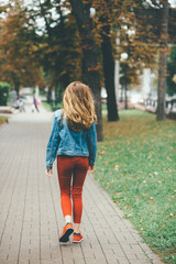 Back view of a blonde girl in red jeans walking in autumn park