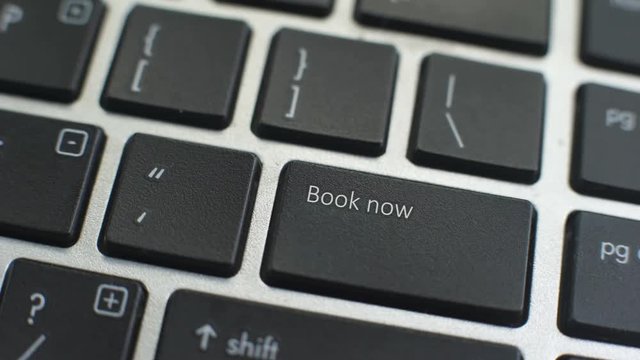 Book now button on computer keyboard, female hand fingers press key