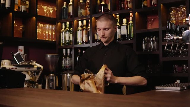 Barman is cleaning the glass with a cloth at bar counter background. The bartender cleaning the glass on the bar