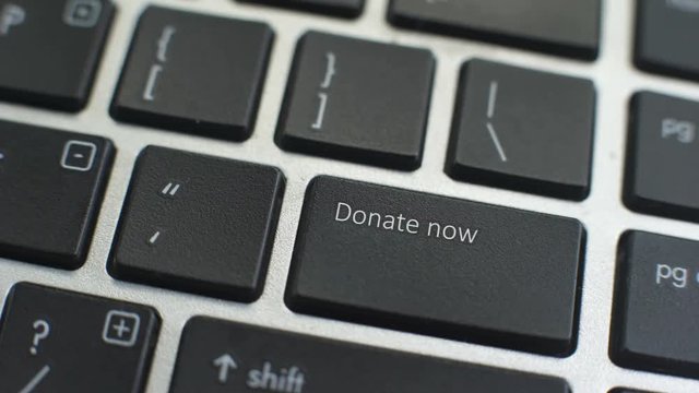 Donate now button on computer keyboard, female hand fingers press key