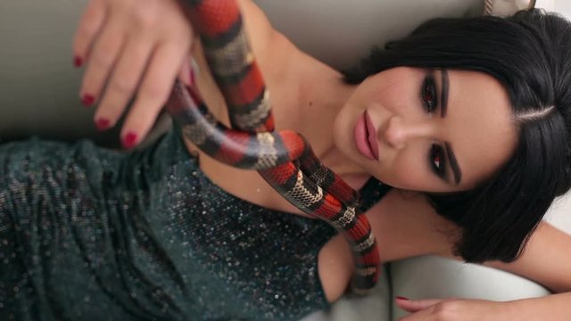 Close-up of a girl with professional make-up is holding a snake in her hands, she wriggles and creeps over her face. Girl model with a snake in the Studio.