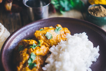 Chicken Tikka Masala (traditional indian curry) with rice and indian bread chapati decorated with spicy red chili peppers, cilantro, Indian spices (turmeric, garam masala) on an old wooden table