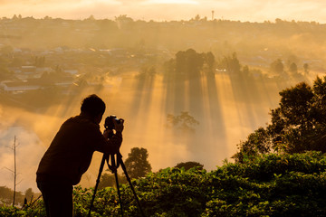 Fototapeta premium Photographer take photos with mirror camera on peak of mountain. misty landscape, spring orange pink misty sunrise in beautiful valley below.