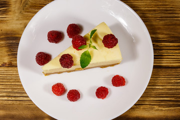 Piece of tasty New York cheesecake with raspberries in a white plate on wooden table. Top view