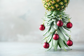 Creative Christmas tree made of pineapple and red bauble on grey concrete background, copy space. Greeting card, decoration for new year party. Holiday concept.
