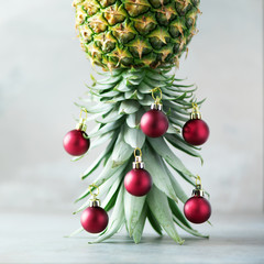 Creative Christmas tree made of pineapple and red bauble on grey concrete background, copy space....