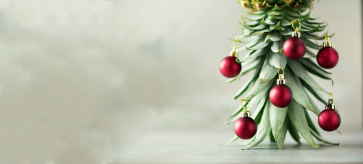 Creative Christmas tree made of pineapple and red bauble on grey concrete background, copy space....