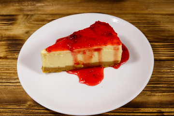 Piece of tasty New York cheesecake with raspberry jam in a white plate on wooden table