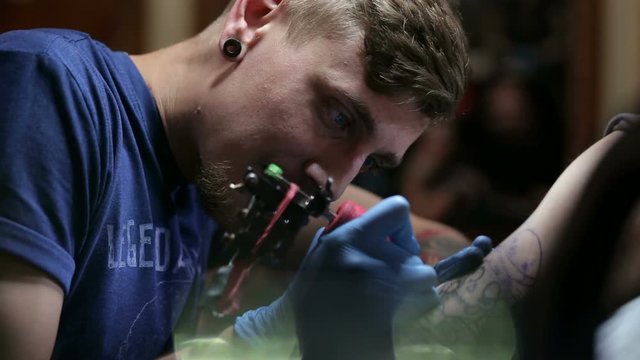 Portrait of a modern tattoo artist while working with a client. A professional tattoo artist makes a tattoo on a man's arm in a tattoo parlor.