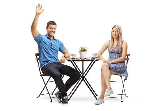 Young couple sitting at a coffee table, the guy waving