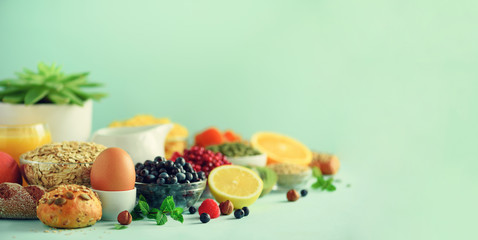 Organic food frame. Banner. Healthy breakfast ingredients. Oat and corn flakes, eggs, nuts, fruits, berries, toast, milk, yogurt, orange, banana, peach on blue background. Top view, copy space