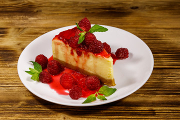 Piece of tasty New York cheesecake with raspberries and raspberry jam in a white plate on wooden table