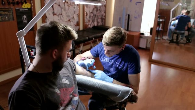 A brutal man makes himself a tattoo in a tattoo parlor. The process of creating a tattoo on the man's arm.