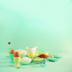 Time to bake. Baking ingredients - butter, sugar, flour, eggs, oil, spoon, rolling pin, brush, whisk, milk over blue background. Bakery food frame, cooking concept. Copy space