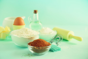 Bakery food frame, cooking concept. Different baking ingredients - butter, sugar, flour, milk, eggs, oil, spoon, rolling pin, brush, whisk over blue background. Copy space
