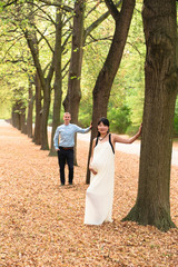Fototapeta premium International family with pregnant woman standing near tree in alley outdoor
