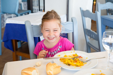 little girl eating paella and laughing in restaurant