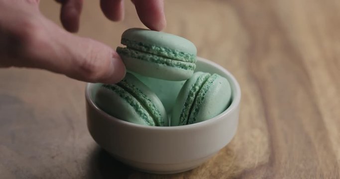 Slow motion man hand put light blue macarons in white bowl on wood table