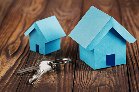 Real  estate concept with small blue toy paper  house and key on wooden background. Idea for real estate concept, personal property and family house.