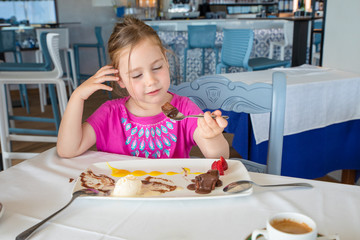smiling little girl eating chocolate dessert in restaurant