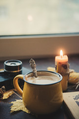 Yellow mug with autumn leaves, a book and candles. The concept of comfort and warmth.