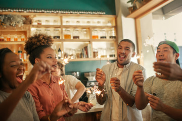 Laughing group of friends celebrating with sparklers in a bar