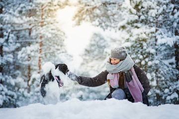 Woman playing with dog in snowy forest. Running and jumping happy pet, girl laughing, having fun. Beautiful winter landscape with trees in snow. 