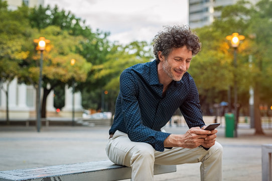 Mature Man Sitting On Bench Using Phone