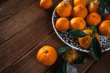Fresh delicious mandarin oranges fruit or tangerines with green leaves in a bowl on wooden background