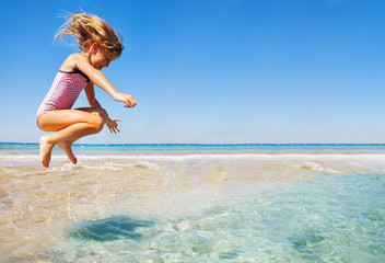 Little girl having fun jumping at shallow water