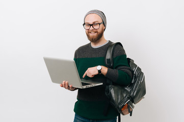 Cheerful young bearded hipster man using laptop over white background and looking at the camera