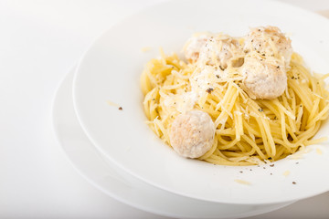 Spaghetti with creamy chicken meatballs served on white plate with pine nuts