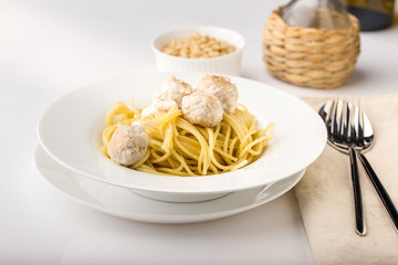 Spaghetti with creamy chicken meatballs served on white plate with pine nuts