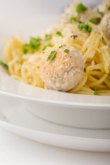 Spaghetti with creamy chicken meatballs served on white plate with pine nuts. Close up