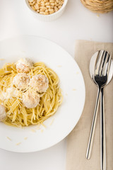 Spaghetti with creamy chicken meatballs served on white plate with pine nuts top view