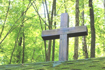 Wooden Christian religious cross on the background of green trees and rays of sunlight at dawn