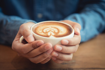 Man hands holding a cup of coffee on wooden table