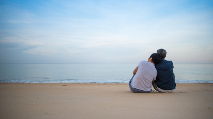 Fototapeta na wymiar Romantic portrait of attractive couple in love hugs sitting on the beach