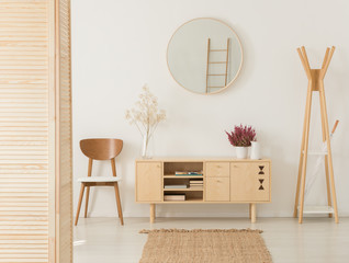 Wooden cabinet with flowers and heather between stylish brown chair and wooden hanger, real photo