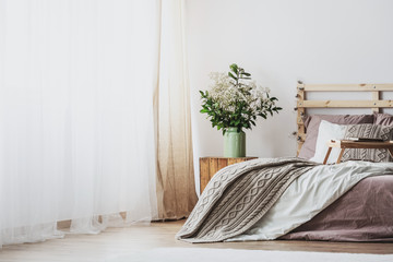 Trendy bedroom interior with comfortable bed with dirty pink bedding and beige warm blanket, real photo with copy space